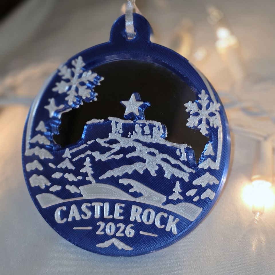 The Castle Rock ornament in Blue: the rock with its star, snowflakes and CASTLE ROCK 2026, and a mirror where the sky is.
