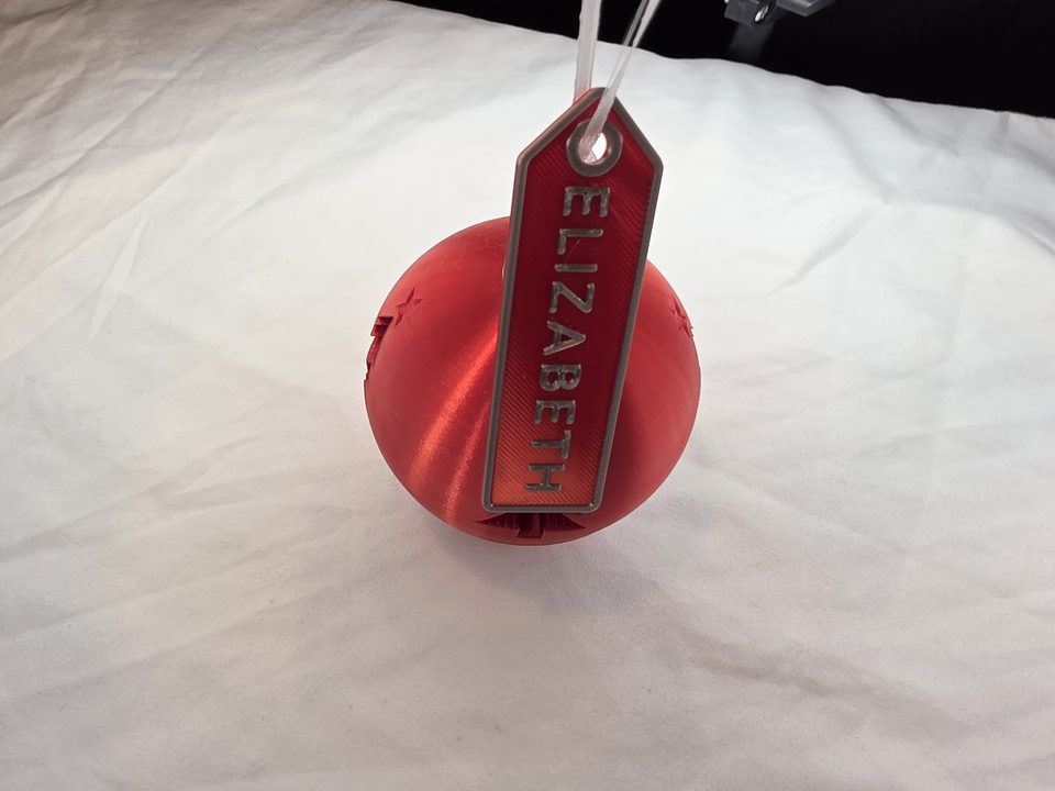 Red Christmas Money Puzzle Ornament with a red and silver name tag that says ELIZABETH, tied to its ribbon.