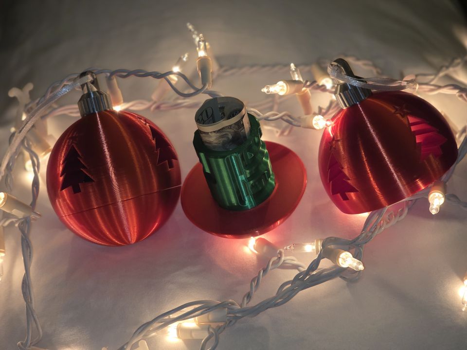 Red Christmas money puzzle ornament opened to show the cash gift inside, next to one closed